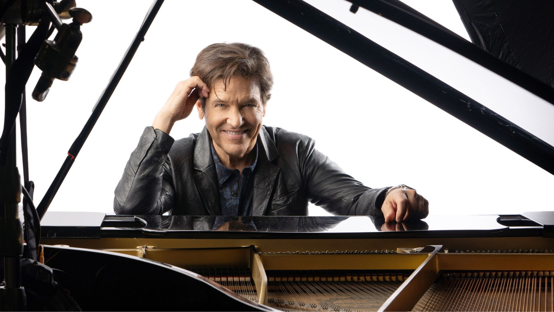 Michael Damian of The Young and the Restless sits at a black piano on a white background